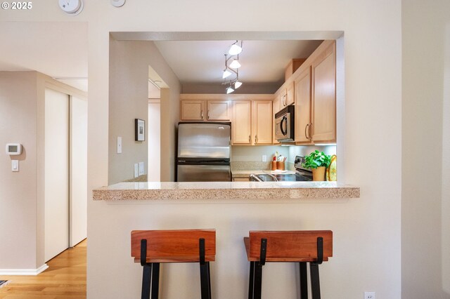 kitchen with light hardwood / wood-style flooring, light brown cabinetry, appliances with stainless steel finishes, a kitchen bar, and kitchen peninsula