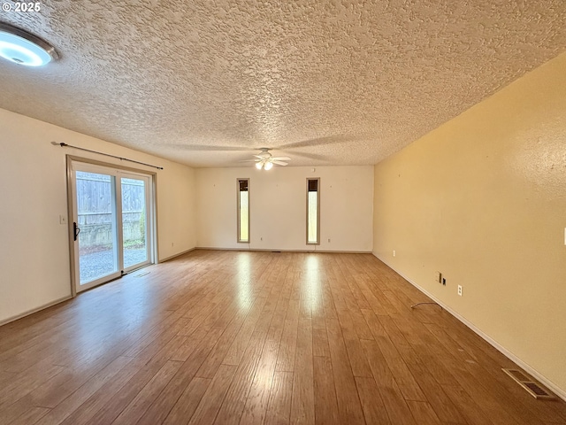 empty room with visible vents, baseboards, a textured ceiling, a ceiling fan, and wood-type flooring