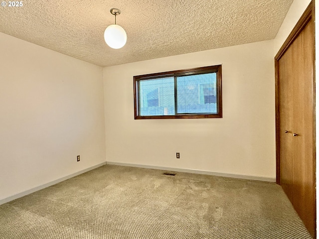 spare room featuring carpet flooring, a textured ceiling, baseboards, and visible vents