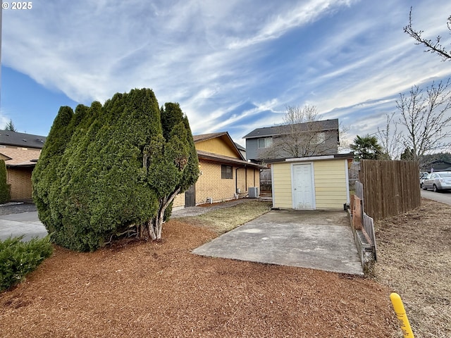 rear view of property featuring central AC, fence, an outdoor structure, brick siding, and a patio area