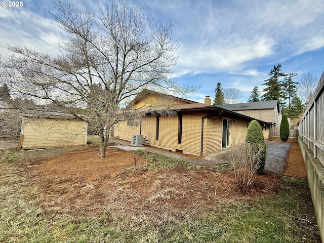 exterior space featuring brick siding, cooling unit, a chimney, and fence