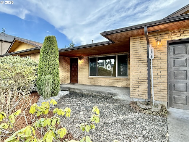 property entrance featuring brick siding, a porch, and an attached garage