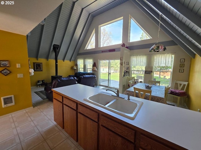 kitchen featuring visible vents, a wood stove, a sink, light countertops, and high vaulted ceiling