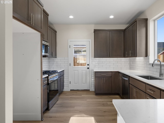 kitchen with sink, appliances with stainless steel finishes, dark brown cabinets, tasteful backsplash, and light hardwood / wood-style floors