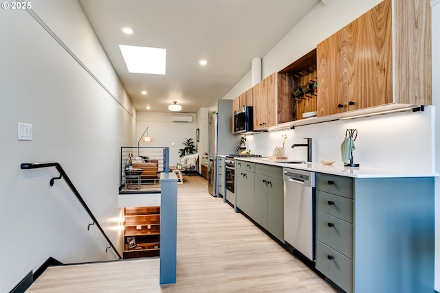 kitchen featuring appliances with stainless steel finishes, a wall mounted air conditioner, a skylight, sink, and light hardwood / wood-style floors