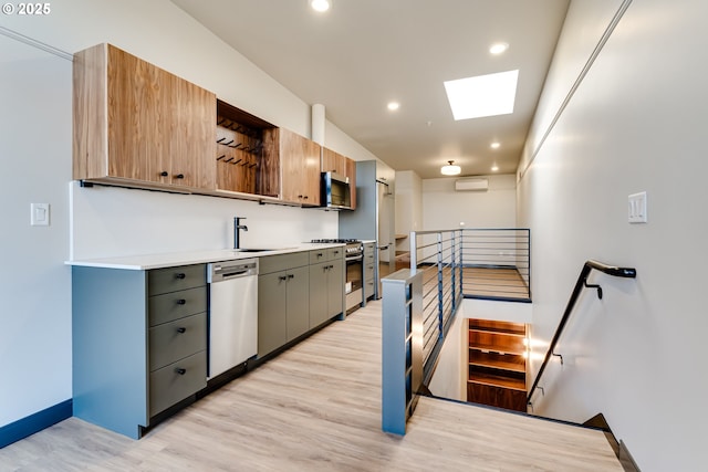 kitchen featuring gray cabinets, a wall mounted air conditioner, a skylight, stainless steel appliances, and light wood-type flooring