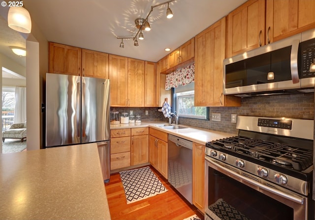 kitchen with tasteful backsplash, light countertops, light wood-style flooring, appliances with stainless steel finishes, and a sink