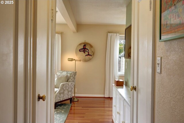 living area featuring light wood-style floors, beam ceiling, and baseboards