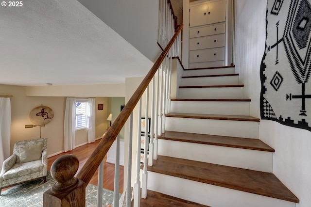 stairs featuring a textured ceiling, wood finished floors, and baseboards