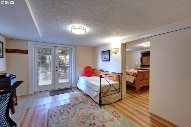 bedroom featuring baseboards, light wood-style flooring, access to outside, a textured ceiling, and french doors