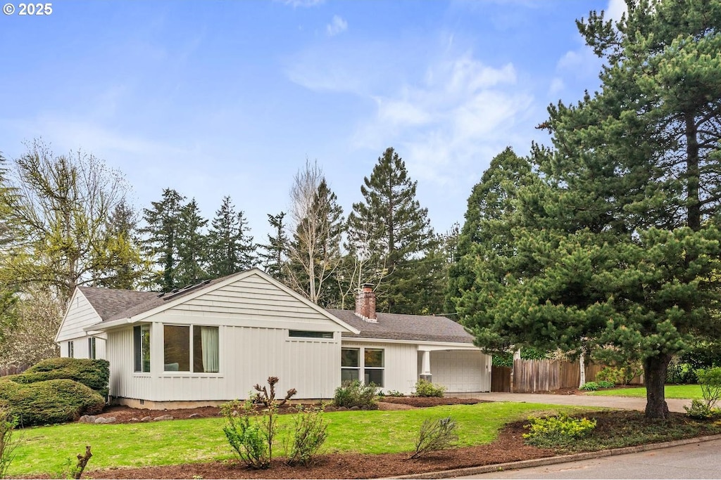 ranch-style house featuring a chimney, fence, concrete driveway, an attached garage, and a front yard
