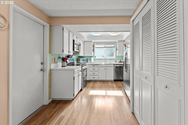 kitchen featuring a textured ceiling, light wood finished floors, appliances with stainless steel finishes, and a sink