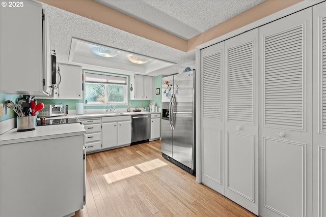 kitchen with light wood finished floors, stainless steel appliances, light countertops, a textured ceiling, and a raised ceiling