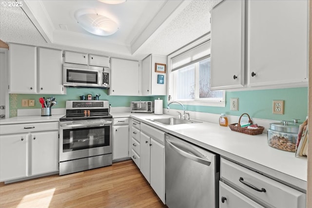 kitchen with light wood finished floors, a sink, stainless steel appliances, light countertops, and a raised ceiling