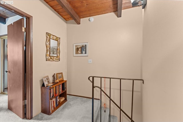 hall featuring an upstairs landing, beamed ceiling, wood ceiling, and carpet