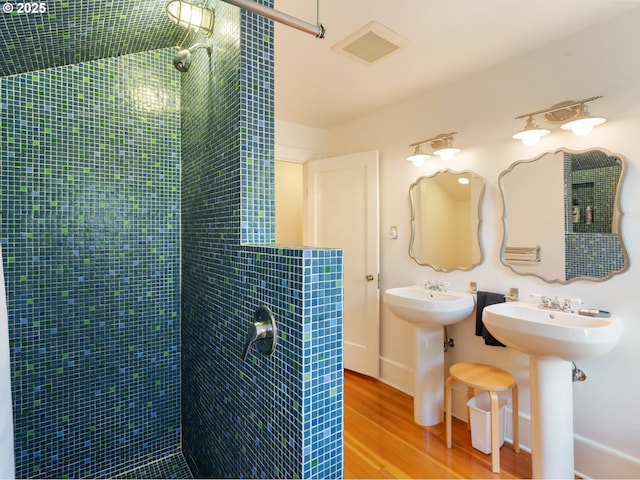 bathroom with wood finished floors, tiled shower, a sink, and baseboards