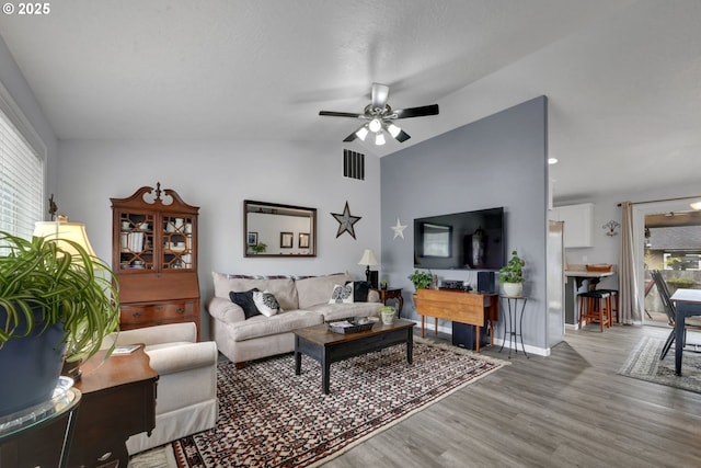 living area featuring wood finished floors, ceiling fan, vaulted ceiling, and baseboards