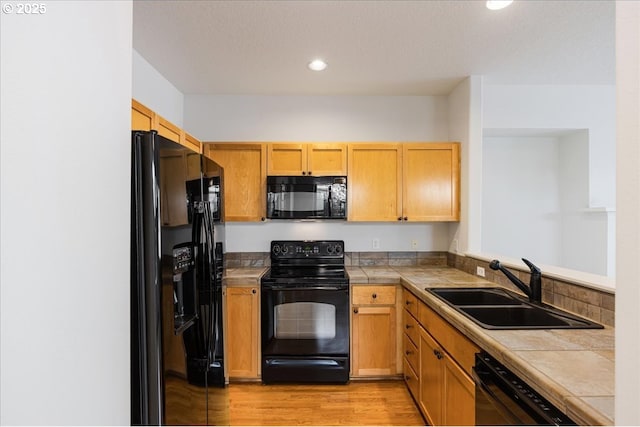 kitchen featuring tile countertops, black appliances, a sink, and light wood-style floors