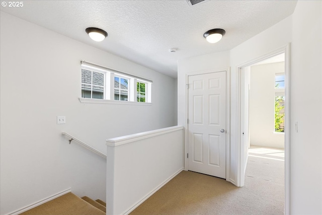 hall with baseboards, carpet flooring, a textured ceiling, and an upstairs landing