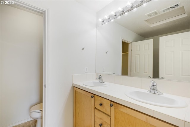 full bath with double vanity, visible vents, toilet, and a sink