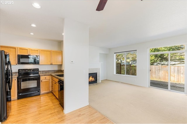 kitchen with light wood-type flooring, open floor plan, light brown cabinets, a tile fireplace, and black appliances