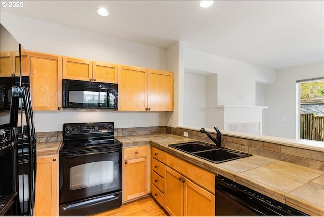 kitchen with a sink, black appliances, light wood-style floors, a peninsula, and recessed lighting