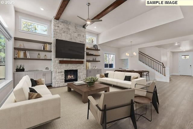 living room with beamed ceiling, light wood-type flooring, ceiling fan with notable chandelier, and a fireplace