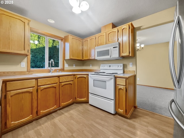 kitchen featuring light wood finished floors, light countertops, a sink, a chandelier, and white appliances