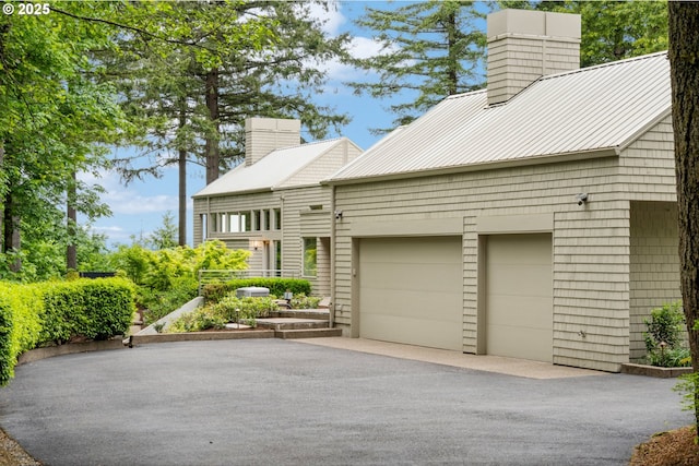 4140 NW Thunder Crest Rd, Portland, OR 97229 - view of property exterior with a chimney, a garage, asphalt driveway, and metal roof