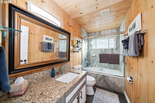 full bathroom featuring vanity, tiled shower / bath combo, wooden walls, and toilet