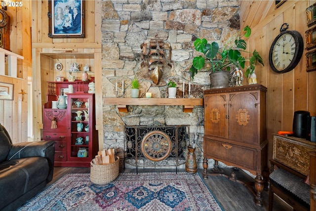 living room featuring a stone fireplace, dark wood-type flooring, and wood walls