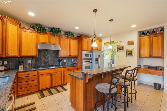 17544 SW Keystone Ct, Beaverton, OR 97007 - kitchen with appliances with stainless steel finishes, under cabinet range hood, light tile patterned floors, brown cabinets, and recessed lighting
