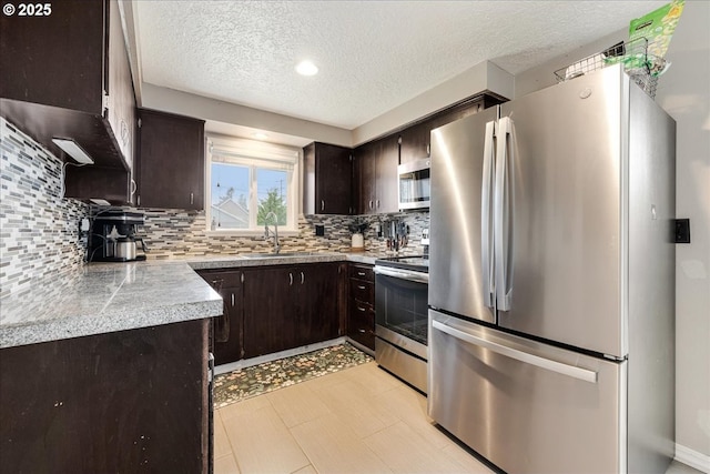 kitchen featuring dark brown cabinetry, tile countertops, appliances with stainless steel finishes, and a sink