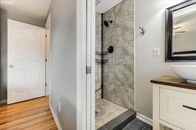 full bathroom with vanity, wood finished floors, baseboards, tiled shower, and a textured ceiling