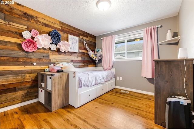 bedroom with visible vents, baseboards, wood walls, wood finished floors, and a textured ceiling