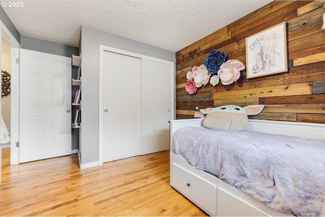 bedroom with light wood-style flooring, a textured ceiling, a closet, and wood walls