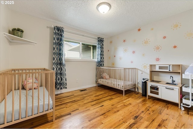 bedroom featuring light wood finished floors, visible vents, wallpapered walls, a textured ceiling, and a sink