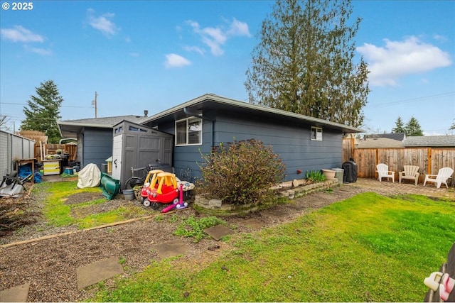 rear view of house featuring an outdoor structure, a storage unit, a fenced backyard, and a lawn