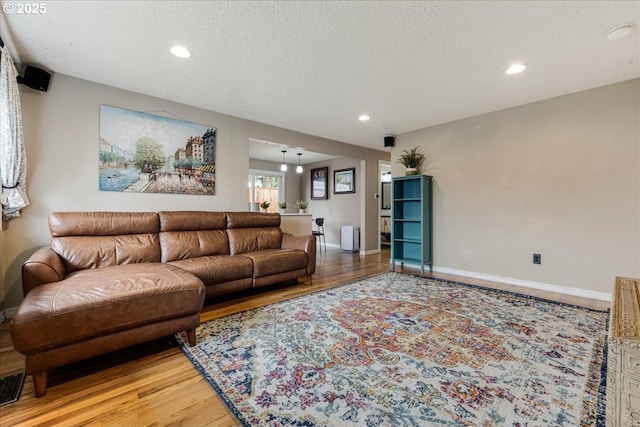 living area with recessed lighting, light wood-style flooring, a textured ceiling, and baseboards