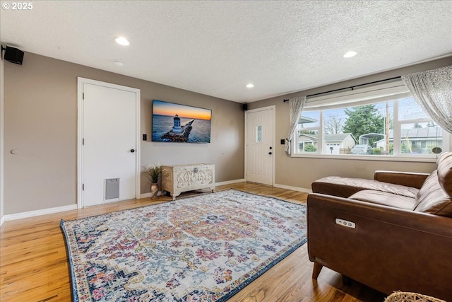 living room featuring recessed lighting, baseboards, a textured ceiling, and light wood-style flooring