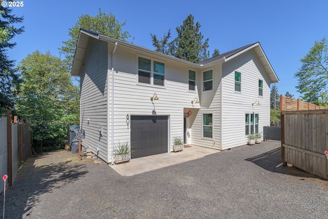 rear view of house with fence, an attached garage, and aphalt driveway