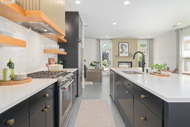 kitchen with appliances with stainless steel finishes, tasteful backsplash, open shelves, a sink, and light countertops