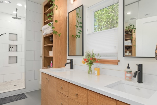 bathroom featuring double vanity, tiled shower, a sink, and visible vents