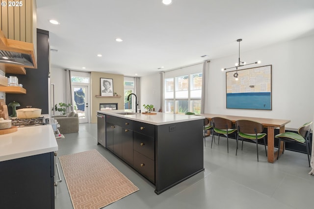 kitchen with a sink, light countertops, dark cabinets, a glass covered fireplace, and open floor plan