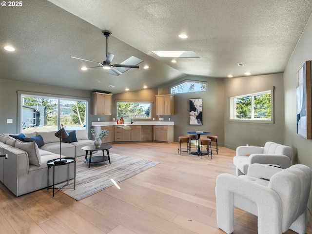 living room featuring a textured ceiling, vaulted ceiling with skylight, ceiling fan, and light hardwood / wood-style flooring