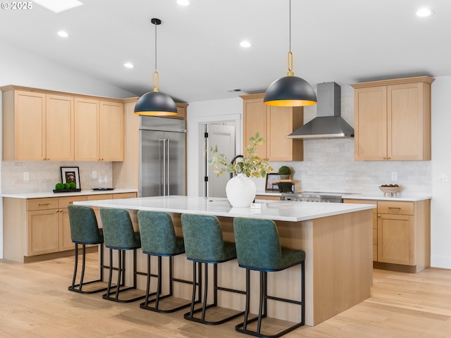 kitchen featuring appliances with stainless steel finishes, a kitchen island with sink, wall chimney range hood, and light brown cabinets