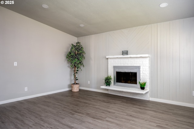 unfurnished living room featuring a brick fireplace, baseboards, and dark wood-style floors