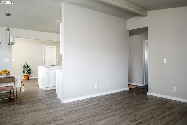 spare room featuring dark wood-type flooring, vaulted ceiling with beams, and baseboards