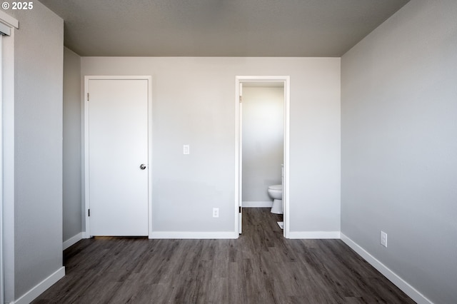 unfurnished bedroom with dark wood finished floors, ensuite bath, and baseboards