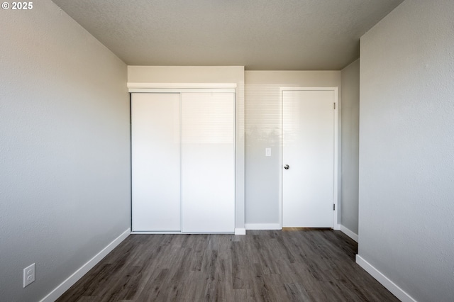 unfurnished bedroom featuring a textured ceiling, baseboards, dark wood finished floors, and a closet